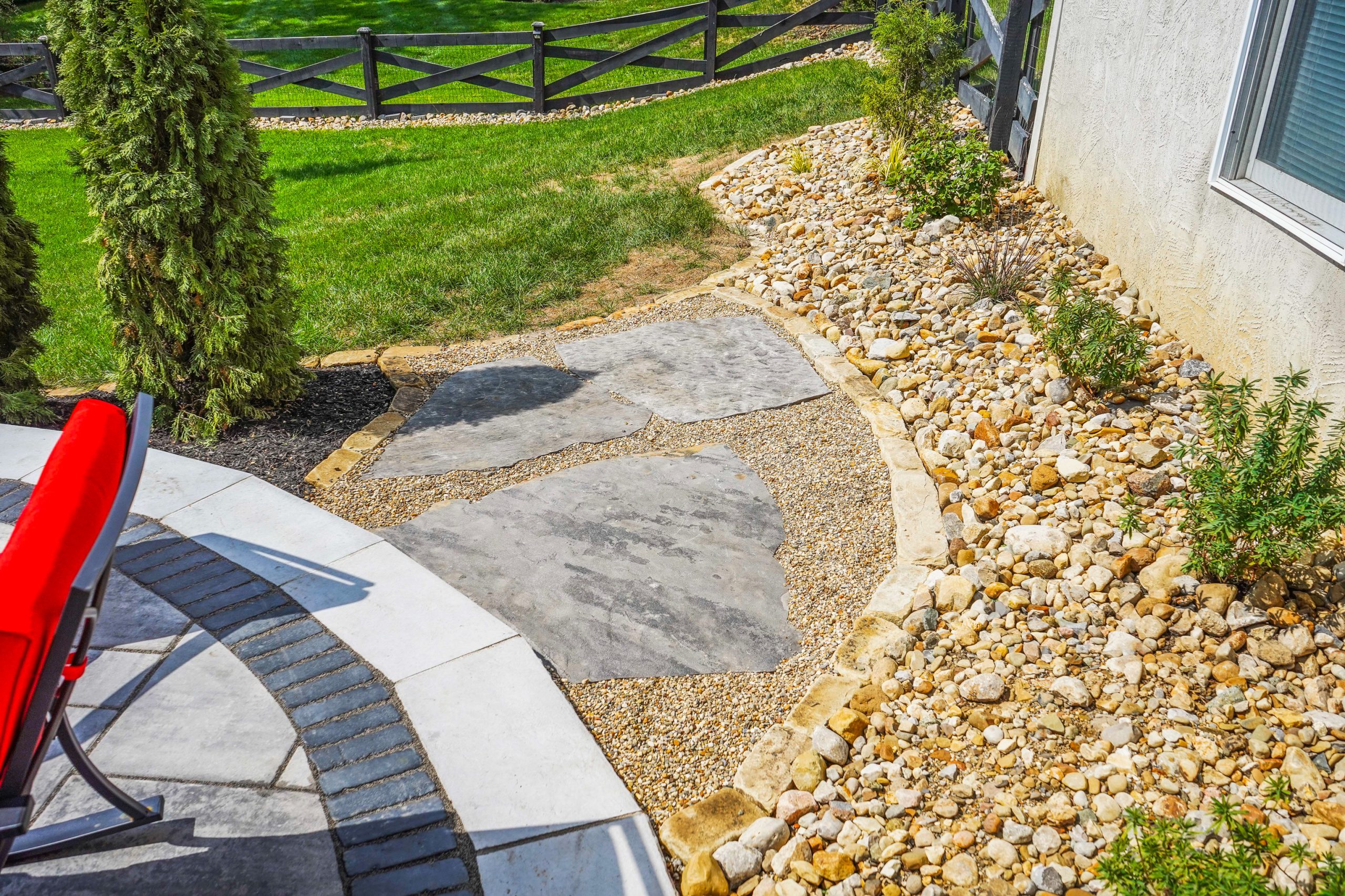 There is walkway to the lawn from deck with shrubs in rock on the side