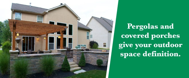 The back of a house with a patio surrounded by a low brick wall and half of the patio covered under a wooden pergola, with a green bar to the right with text reading "Pergolas and covered porches give your outdoor space definition."