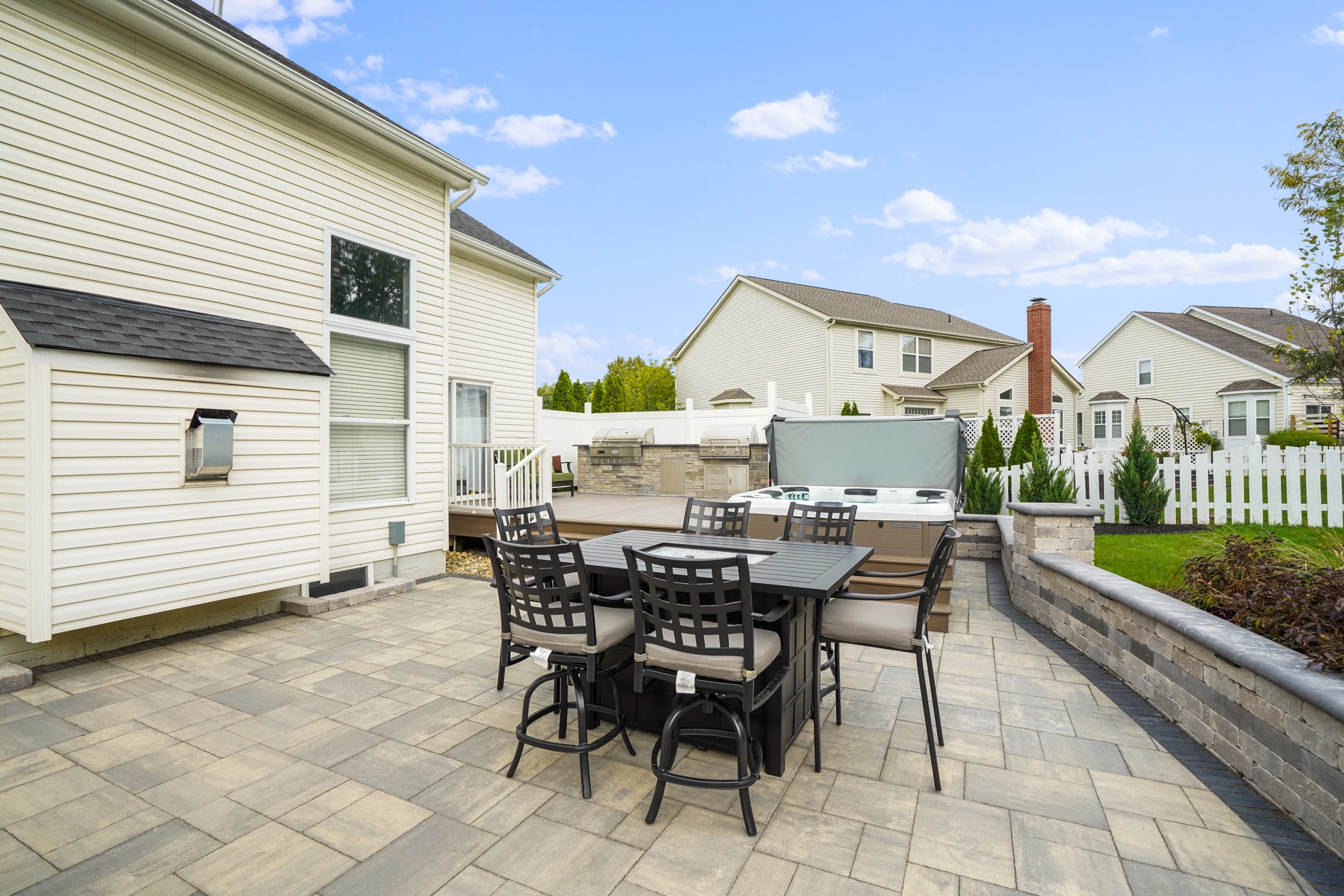 Side-by-side jacuzzi and kitchen on deck with neighbor homes behind. There is a shrub and lawn behind the retaining wall but within the fence.