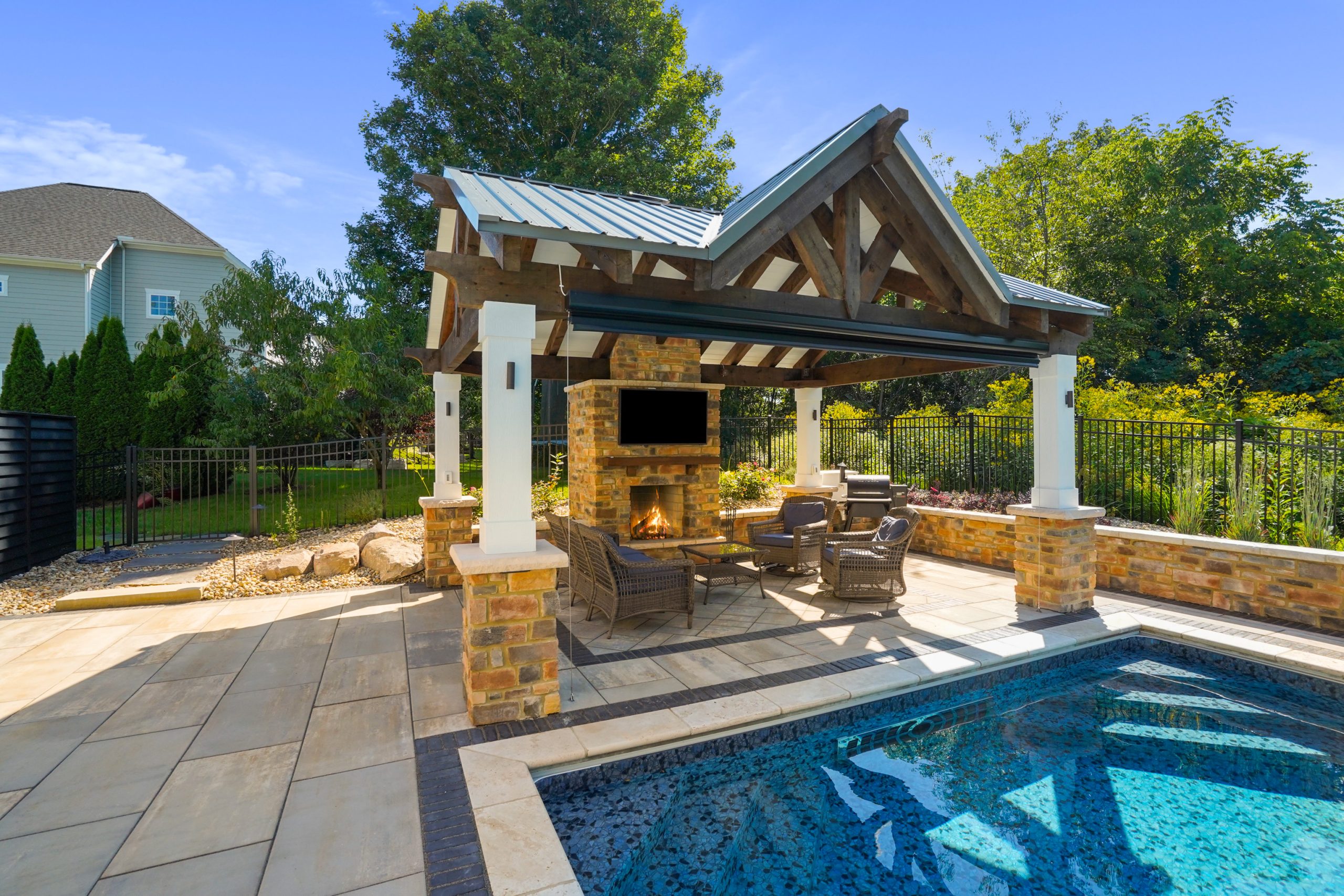 Detached patio fireplace around pool within fenced area and green vegetation outside fenced area