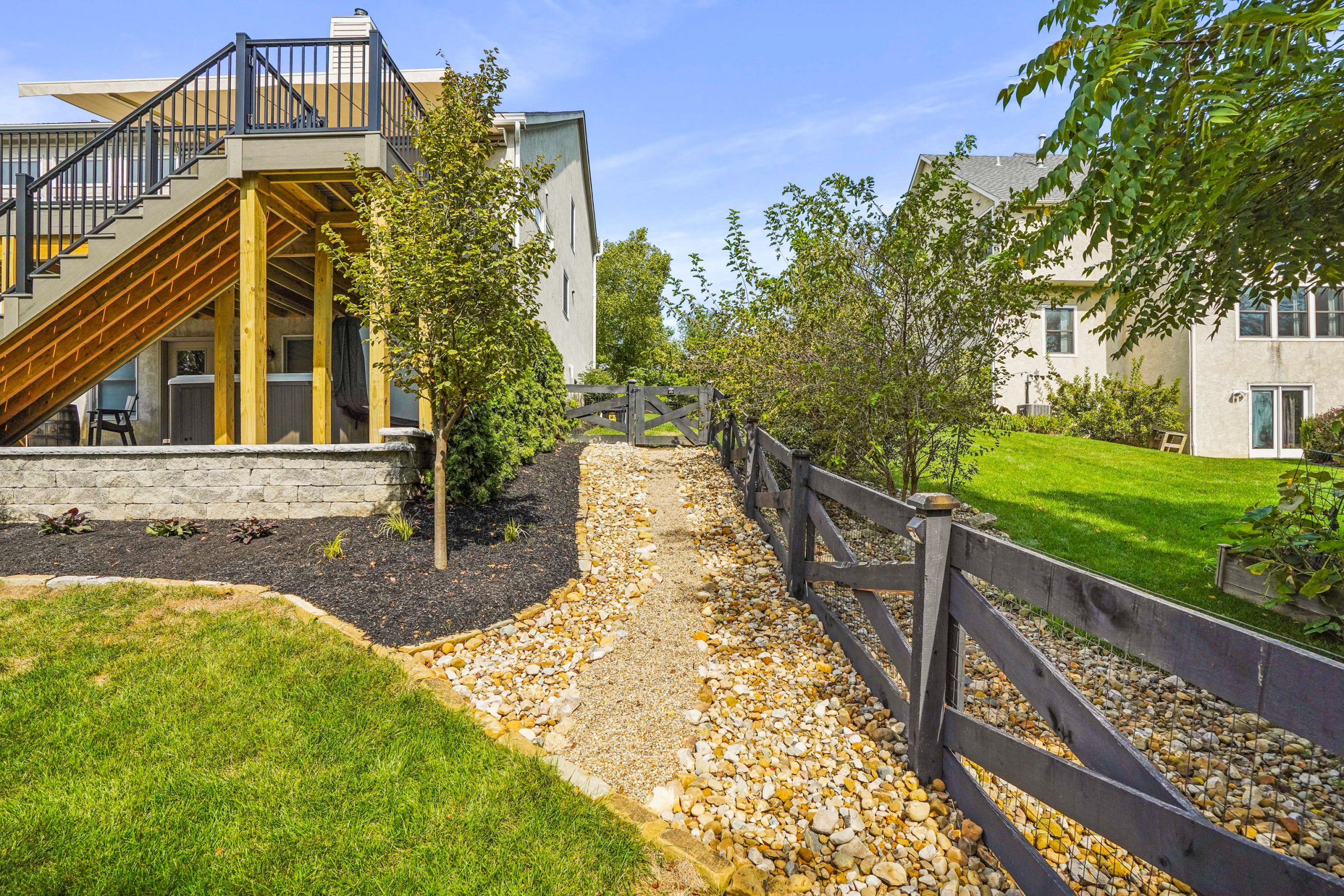 Side view of home with trees, lawn and rock walkway on property. To the right is lawn and trees on neighbor's property.