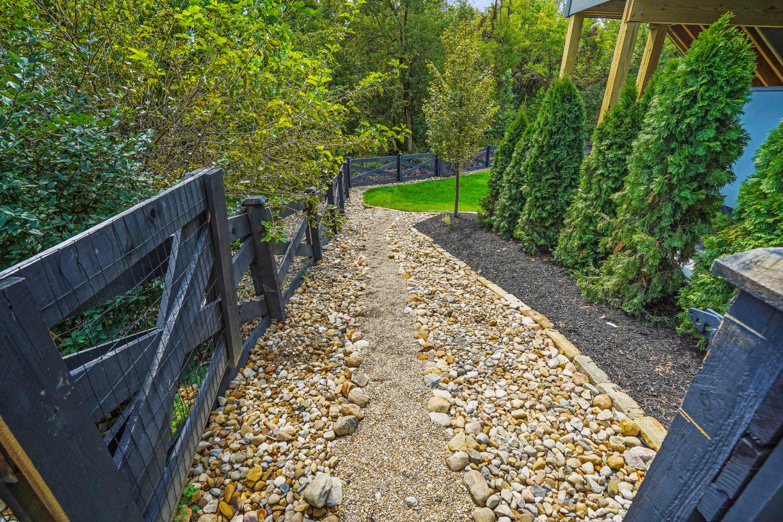 open door to walkway hardscape with tress on the left and hedges on the right.