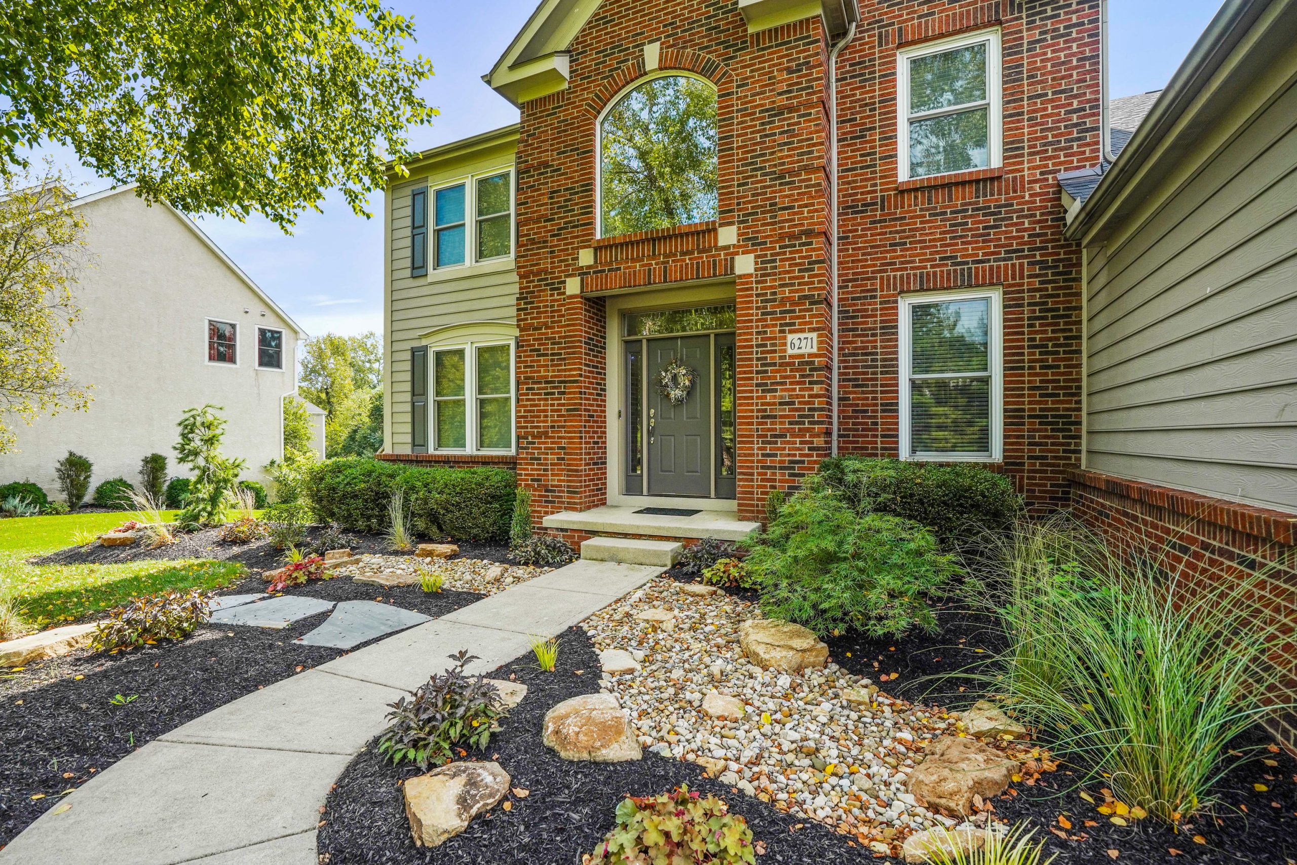 Red brick home entrance decorated with shrubs and has a lawn.