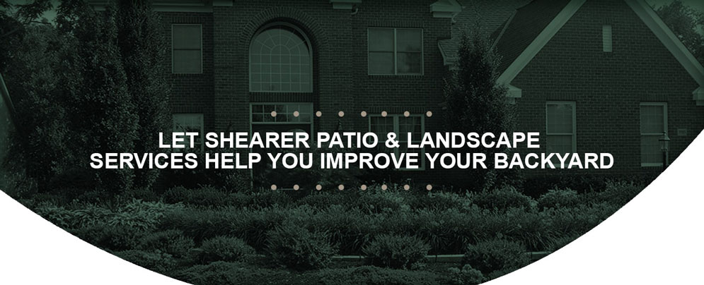 A green toned shot of the front of a house fully decorated with greenery of trees and bushes, all set to the background with text overtop which reads "Let Shearer Patio & Landscape Services Help You Improve Your Backyard"