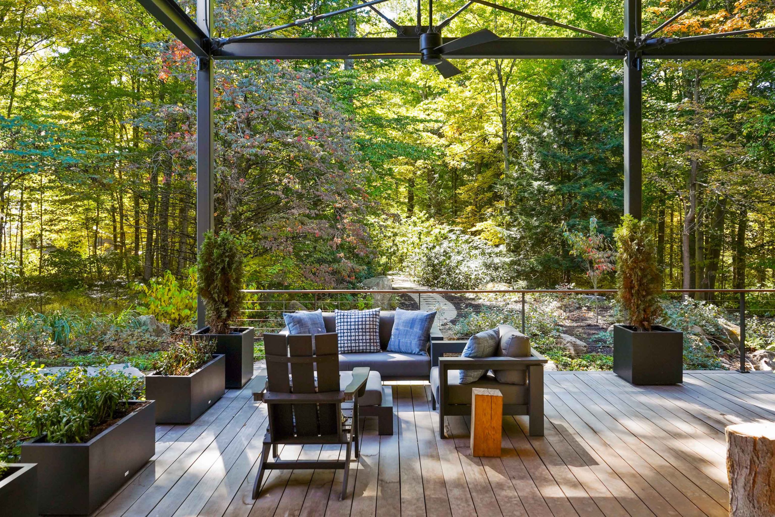 Patio with comfy chairs and plant vases is surrounded by colorful trees