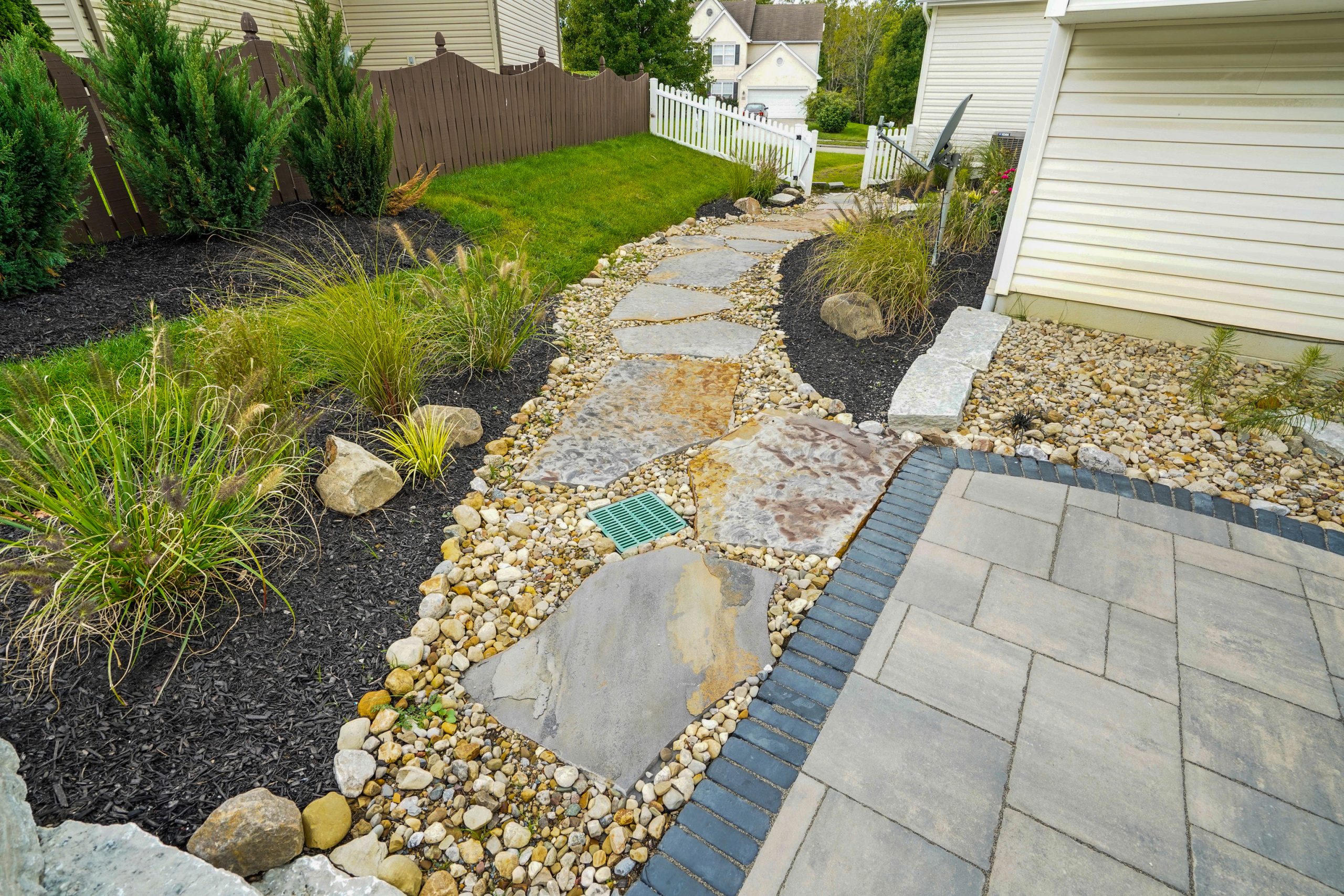 Walkway hardscape surrounded by lawn and shrubs on fenced property.