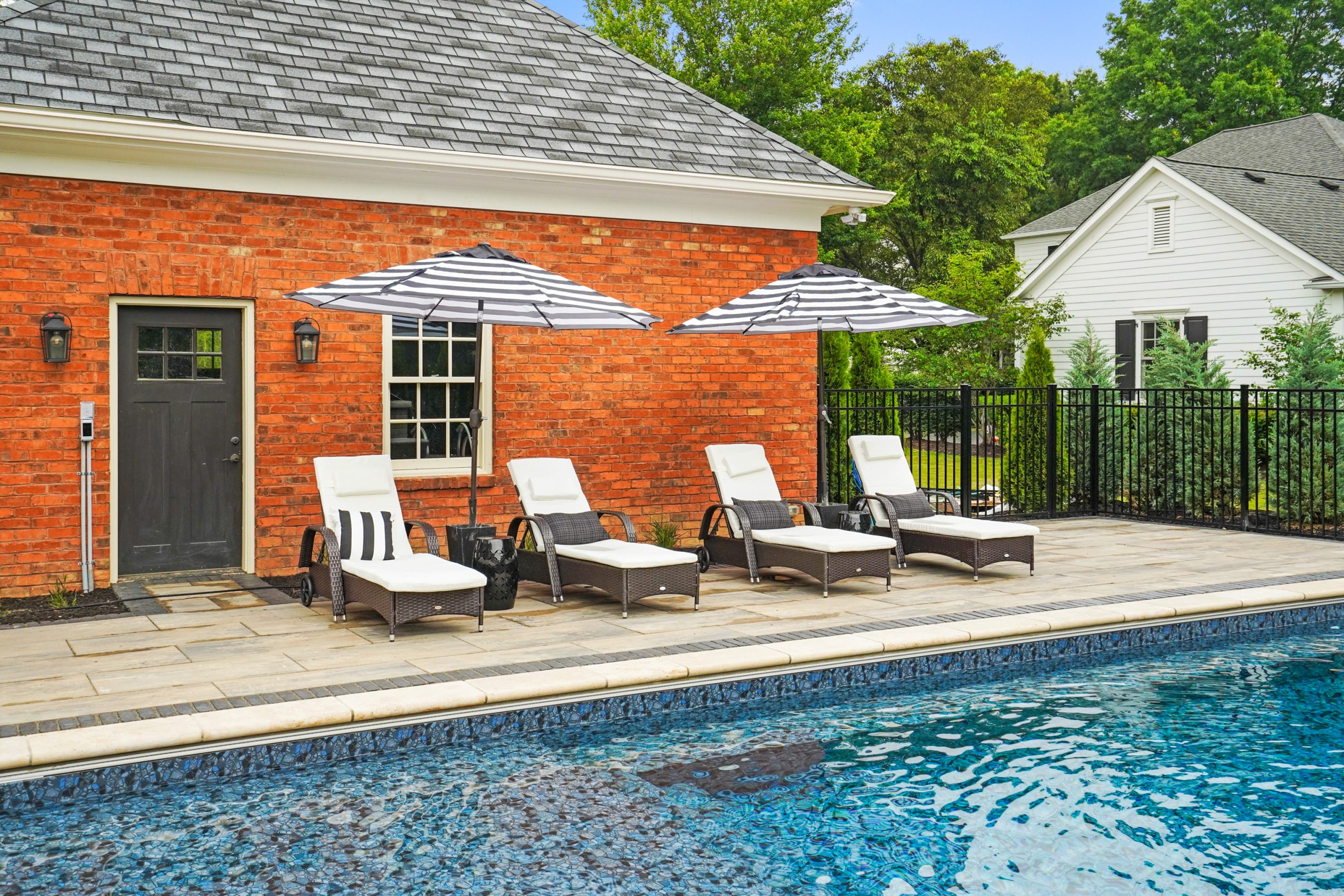 Pool with umbrella chairs within a fence and trees outside the fence